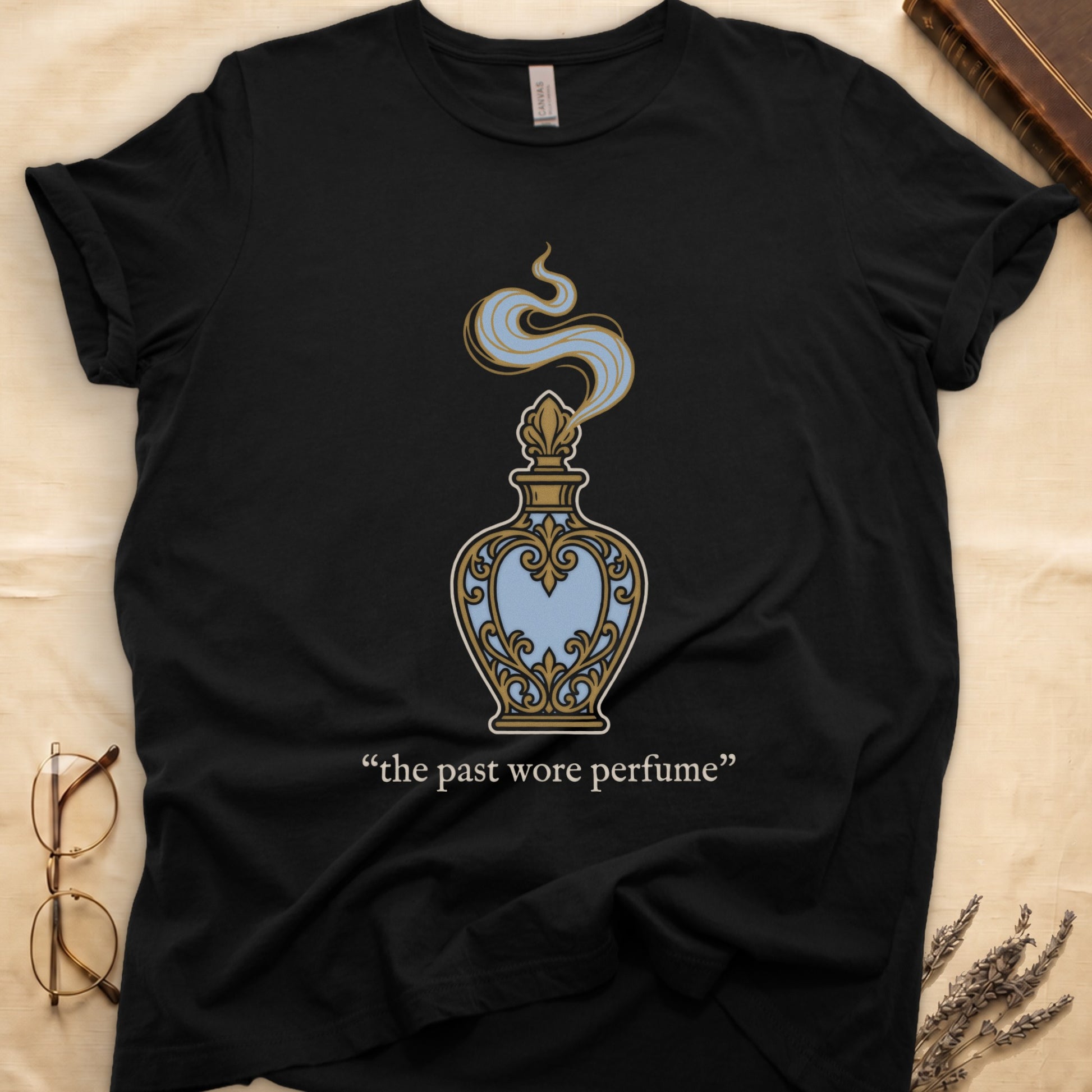 Black tee with ornate blue and gold perfume bottle, rising scent swirl, "the past wore perfume" cream serif below.
