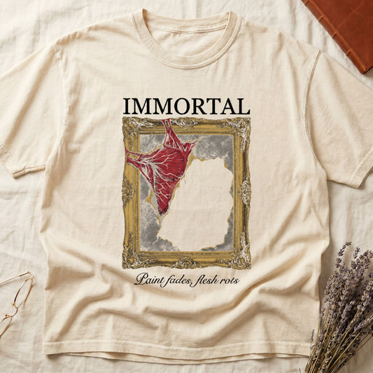 Ivory tee with gold frame and exposed muscle tearing canvas, "IMMORTAL" top, "Paint fades, flesh rots" italic below.