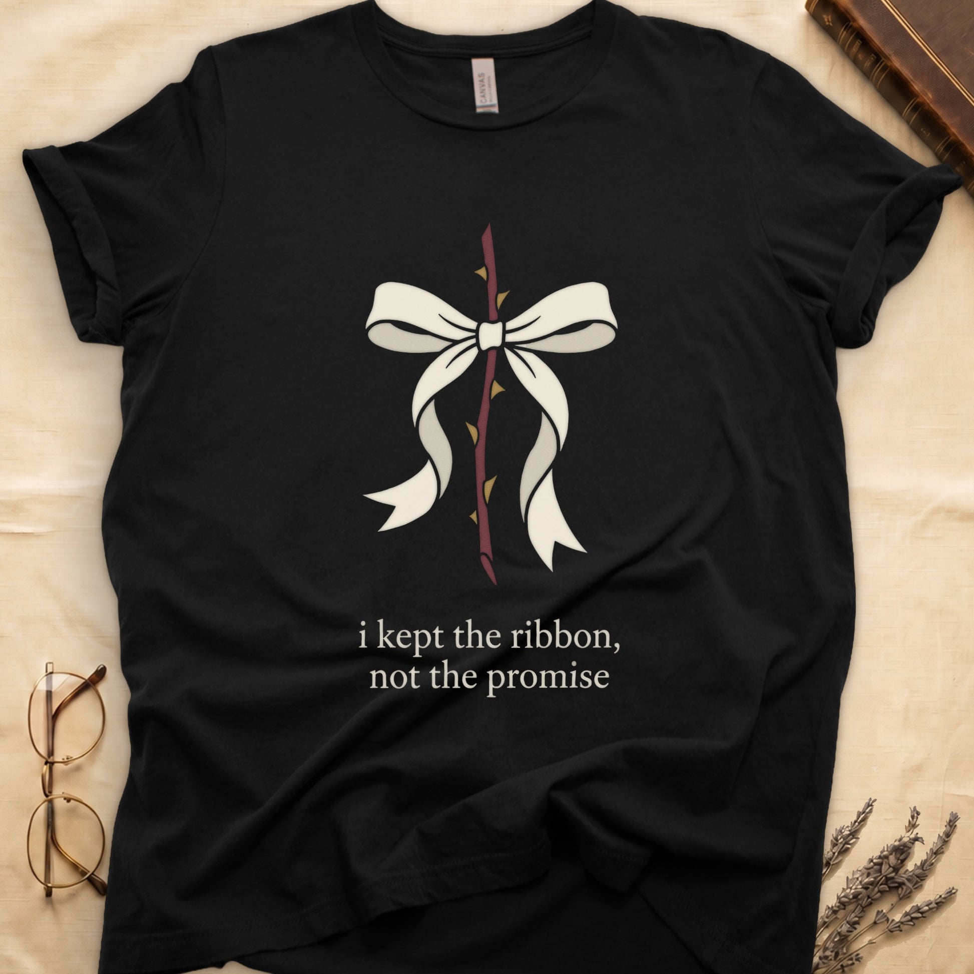 Black tee with cream bow tied around thorny rose stem, "i kept the ribbon, not the promise" in cream serif below.