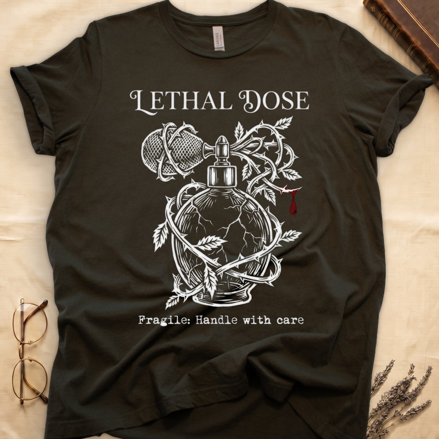 Military Green tee with cracked perfume bottle wrapped in thorns, blood drop, "LETHAL DOSE" top, "Fragile: Handle with care" below.