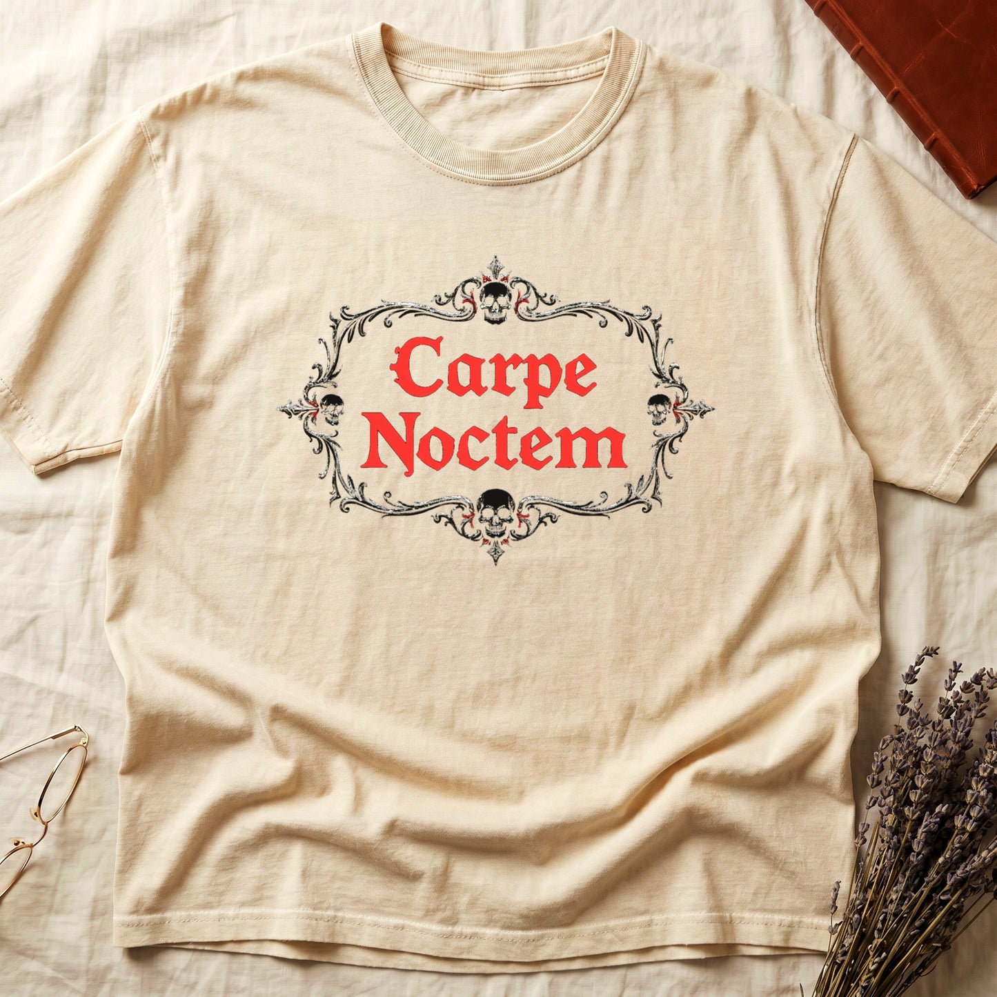 Ivory tee with silver filigree cartouche, crowned skull top and skull below, "Carpe Noctem" in deep-red blackletter inside.