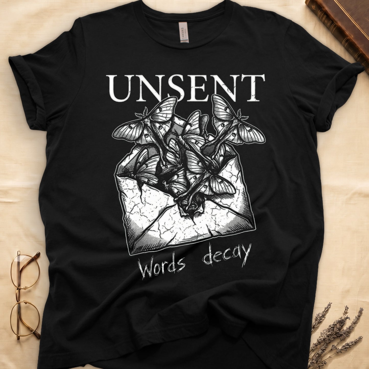 Black tee with 'UNSENT' in serif type, 'Words decay' brush text, luna moths from torn envelope in crosshatched ink