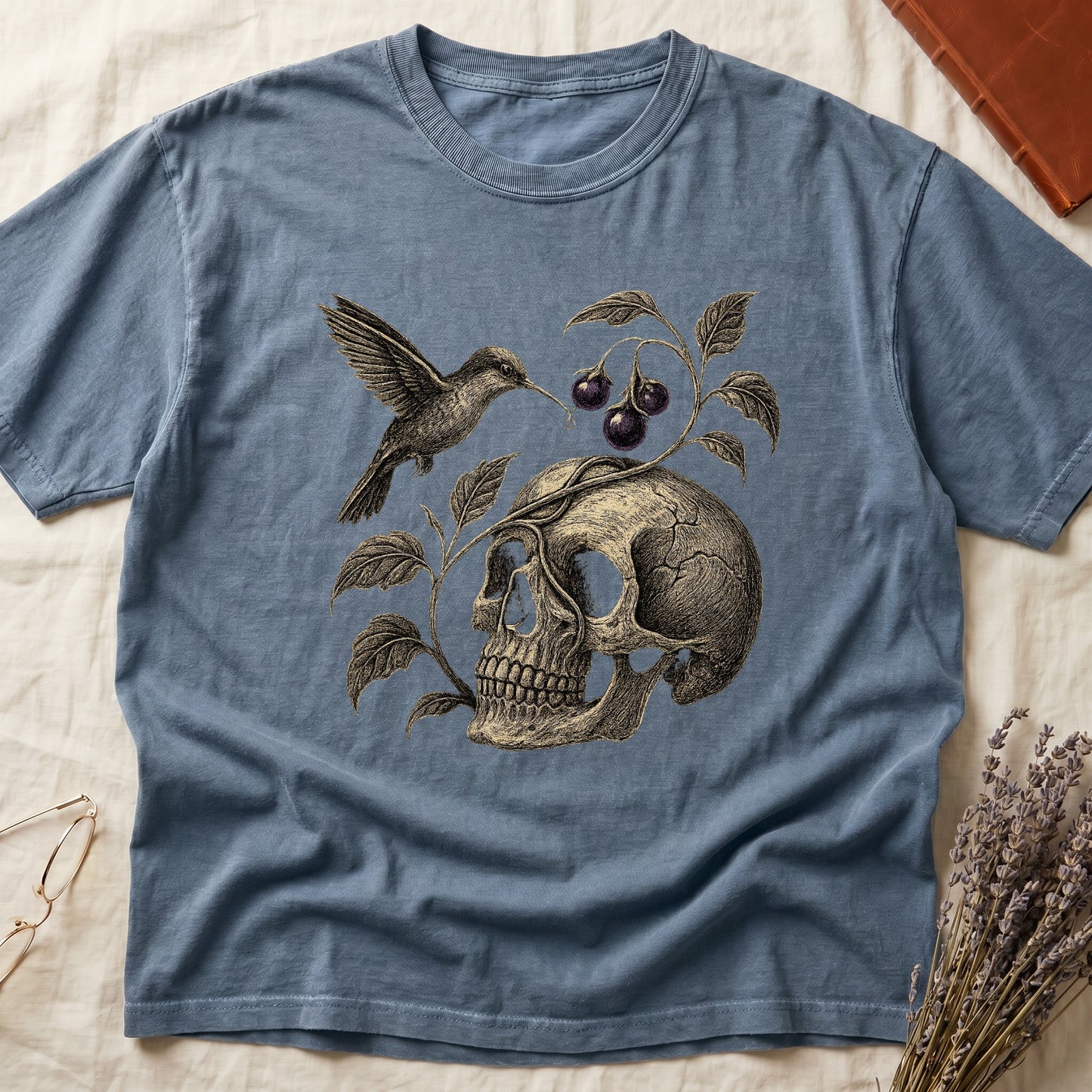 Blue Jean tee with sepia engraved skull, nightshade vine and dark-purple berries wrapping around, hummingbird at upper left.