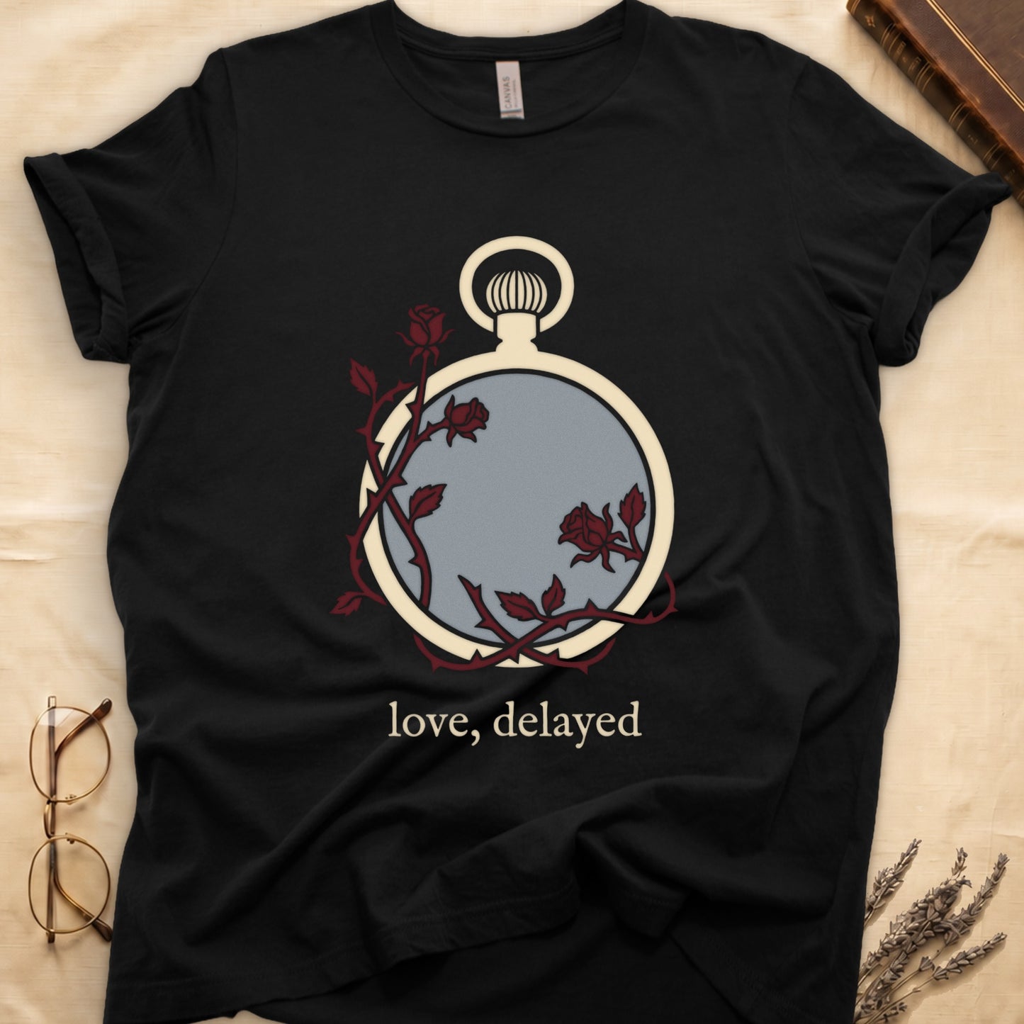 Black tee with vintage cream pocket watch and dark red roses entwined, "love, delayed" in cream serif below.