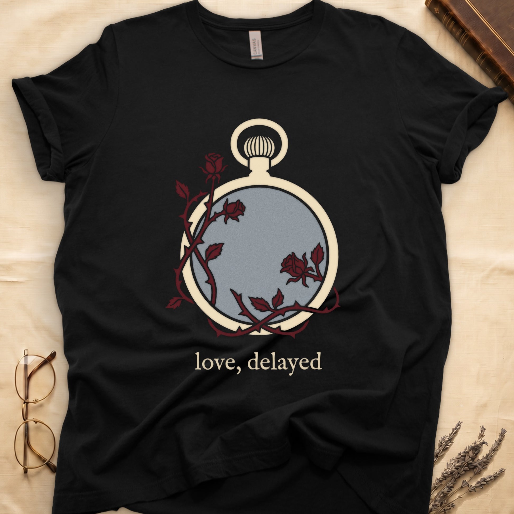Black tee with vintage cream pocket watch and dark red roses entwined, "love, delayed" in cream serif below.