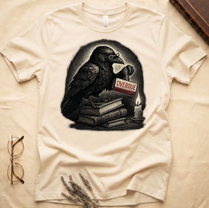 Natural tee with bespectacled raven on stacked books, holding wooden "OVERDUE" stamp, lit candle beside, dawn glow behind.