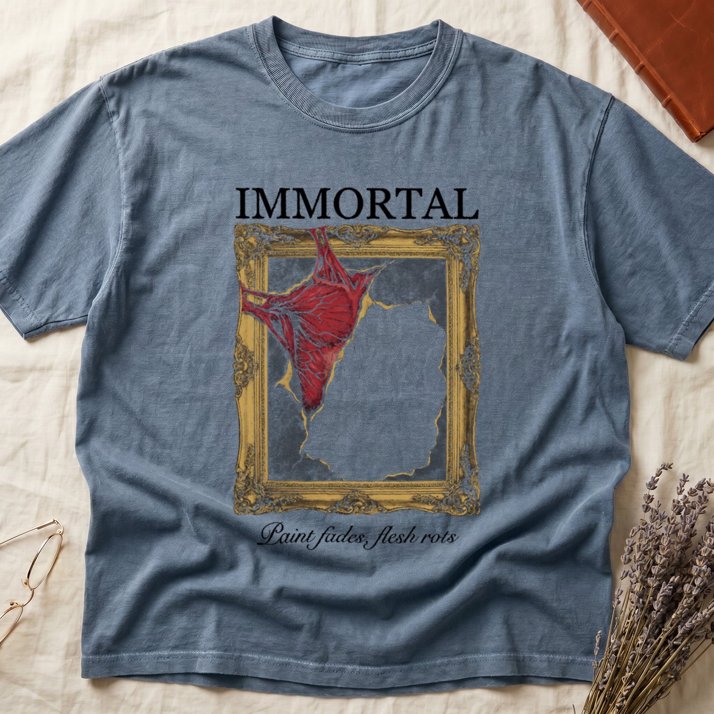 Blue Jean tee with gold frame and exposed muscle tearing canvas, "IMMORTAL" top, "Paint fades, flesh rots" italic below.