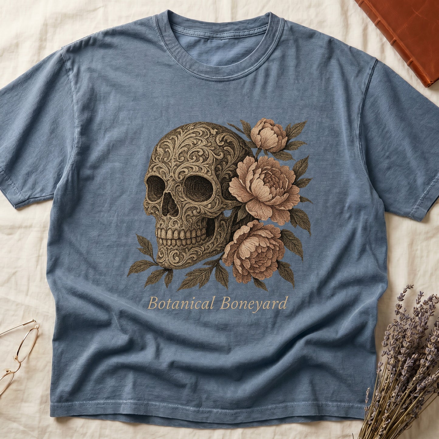 Blue Jean tee with filigree-engraved skull on left, peach-cream peonies on right, crossed bones below, "Botanical Boneyard."