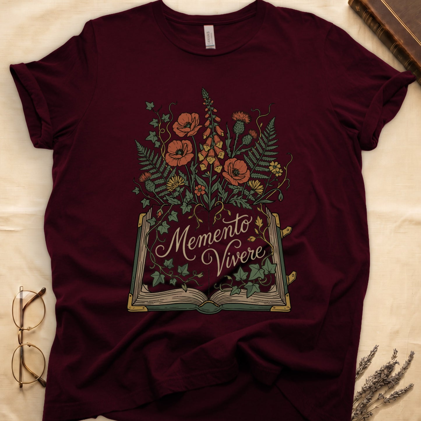 Maroon tee with open book and botanical illustration, red poppies, golden foxglove, ferns and ivy spilling from the pages.