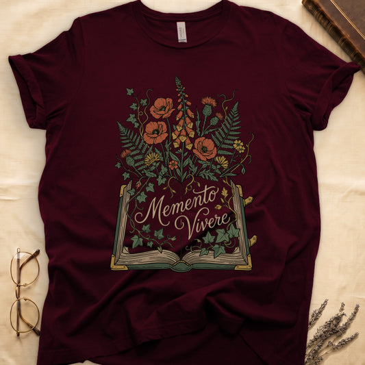 Maroon tee with open book and botanical illustration, red poppies, golden foxglove, ferns and ivy spilling from the pages.