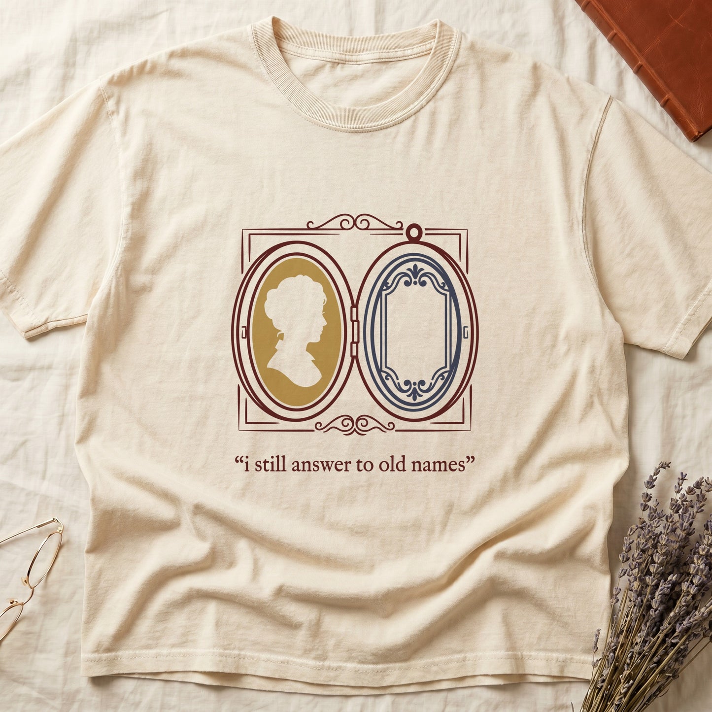 Ivory tee with Victorian double-locket, silhouette portrait in gold frame, "i still answer to old names" cream serif below.