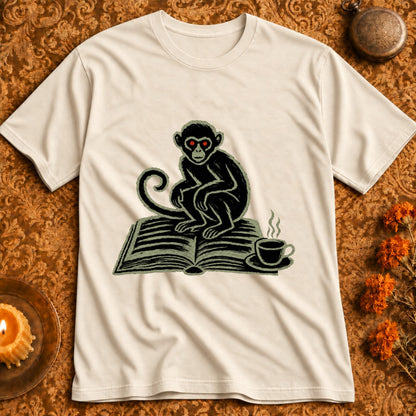 Cream t-shirt with a black monkey with red eyes sitting on an open book next to a steaming coffee cup.