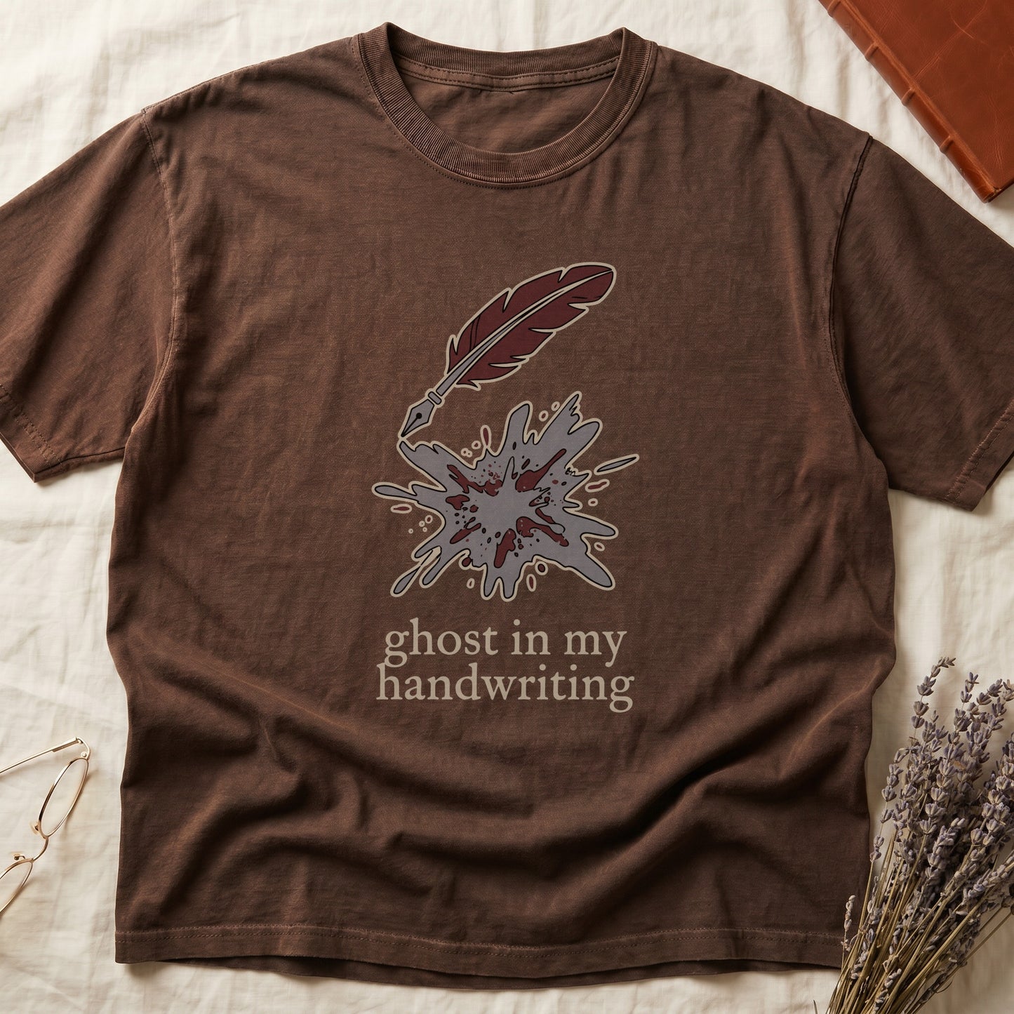 Espresso tee with burgundy quill pen and grey ink splatter, "ghost in my handwriting" cream serif below.
