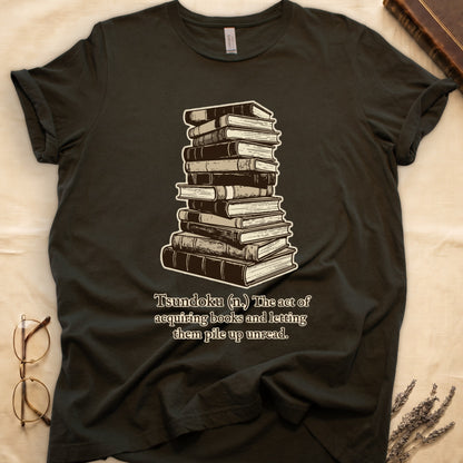 Military Green tee with stack of vintage hardcovers, "Tsundoku (n.) The act of acquiring books and letting them pile up unread."