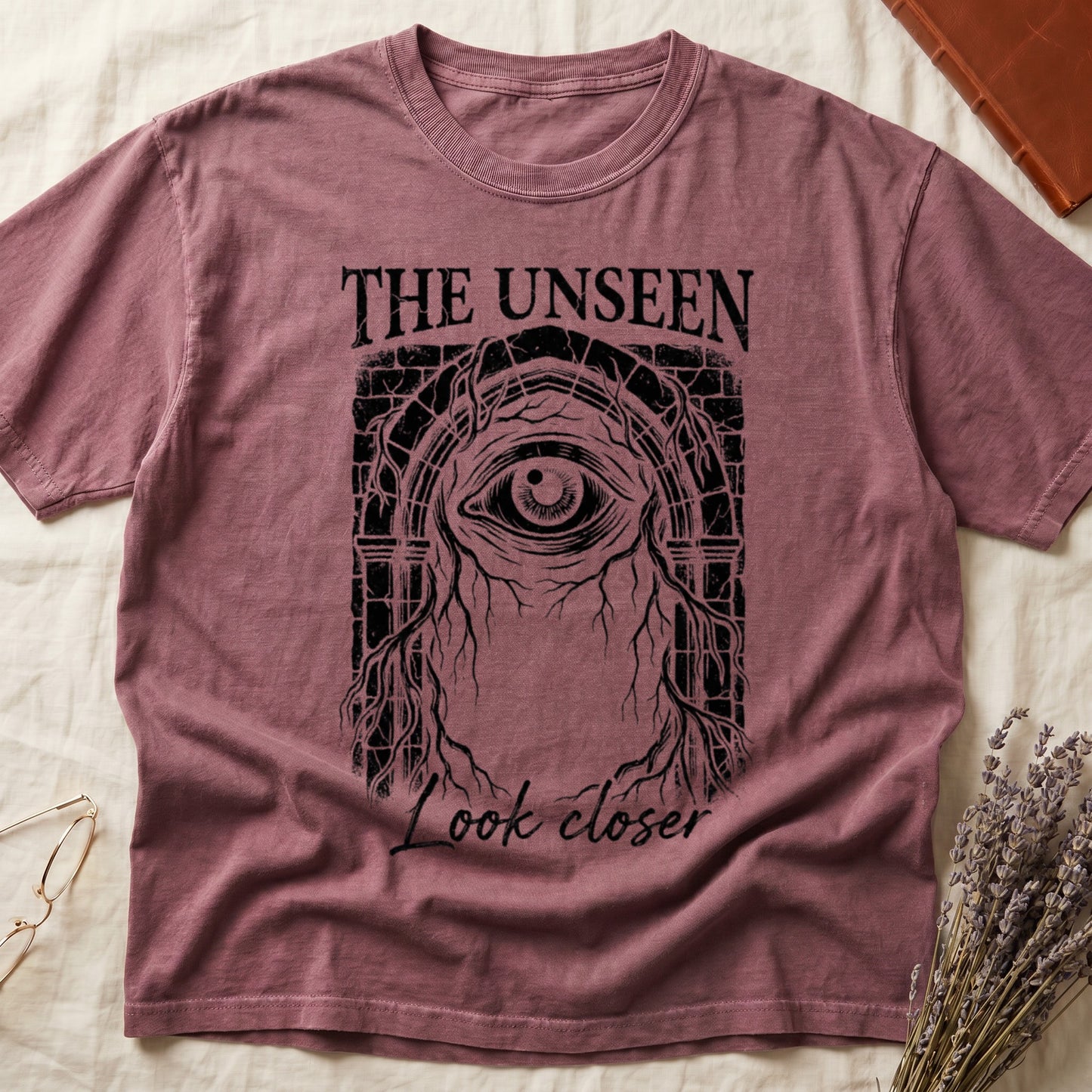Dark Rose tee with Gothic stone arch, open eye, roots trailing, "THE UNSEEN" top, "Look closer" cursive below.