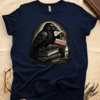 Navy tee with bespectacled raven on stacked books, holding wooden "OVERDUE" stamp, lit candle beside, dawn glow behind.