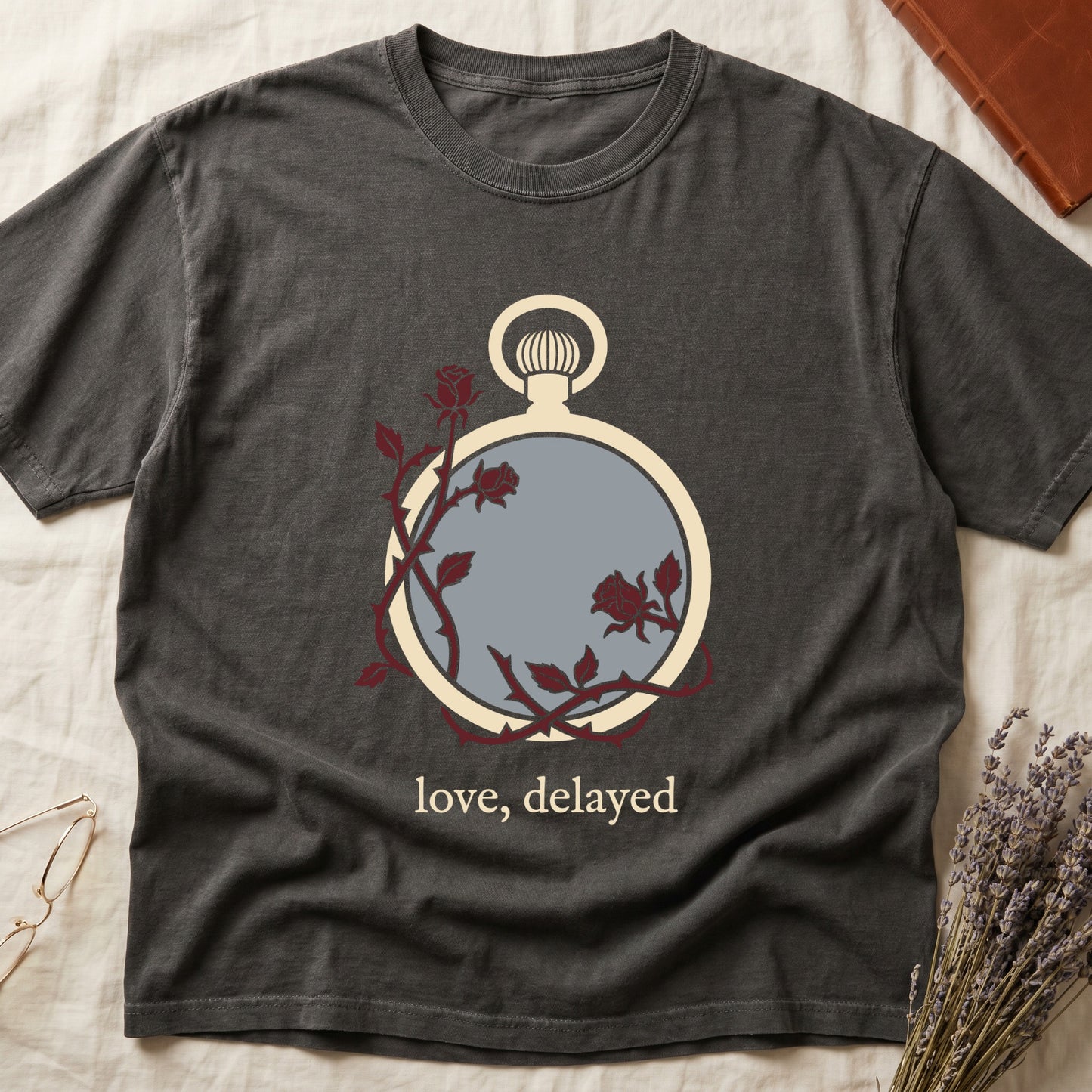Pepper tee with vintage cream pocket watch and dark red roses entwined, "love, delayed" in cream serif below.