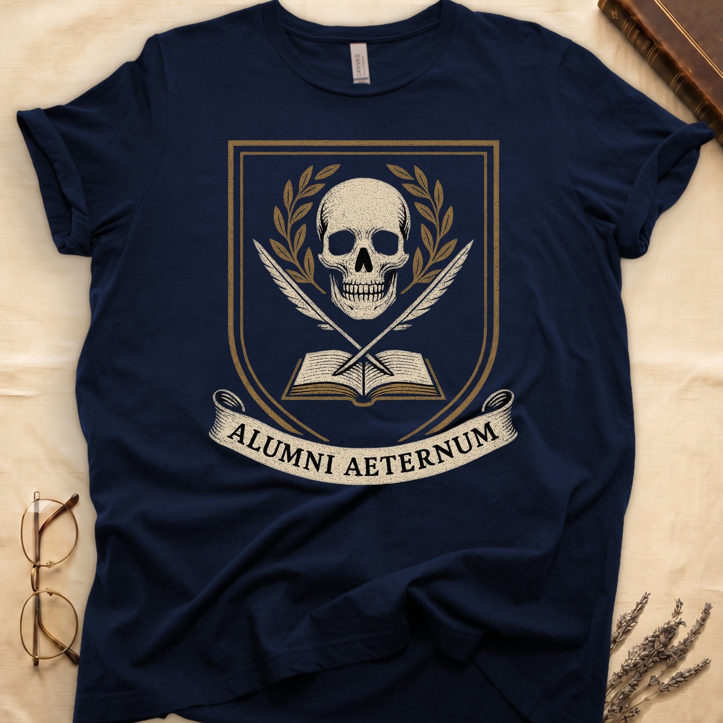 Navy tee with heraldic shield, skull and gold laurels, crossed quills, open book, scroll "ALUMNI AETERNUM" below.