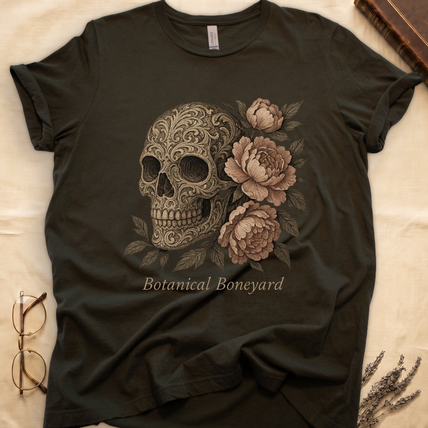 Military Green tee with filigree-engraved skull on left, peach-cream peonies on right, crossed bones below, "Botanical Boneyard."
