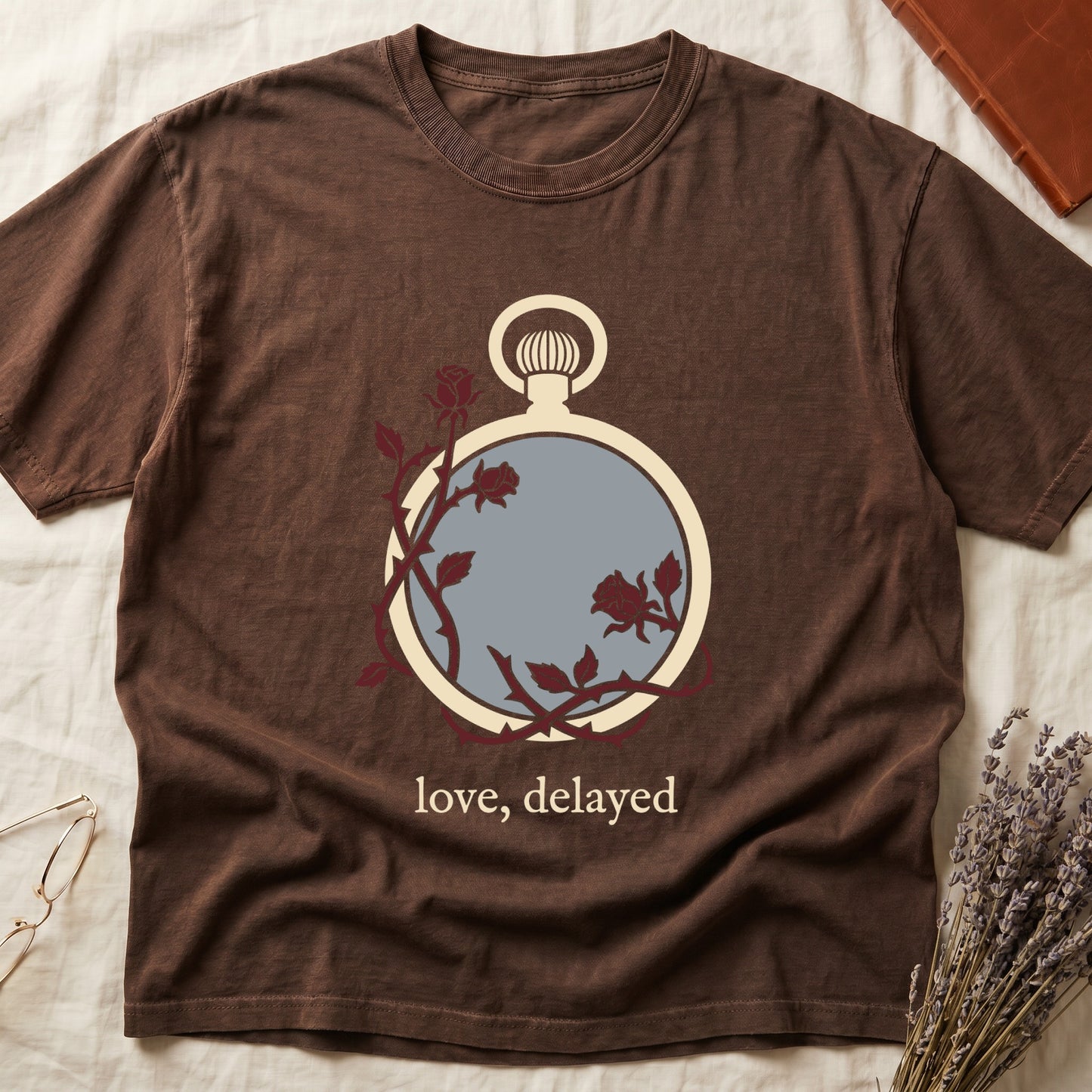 Espresso tee with vintage cream pocket watch and dark red roses entwined, "love, delayed" in cream serif below.