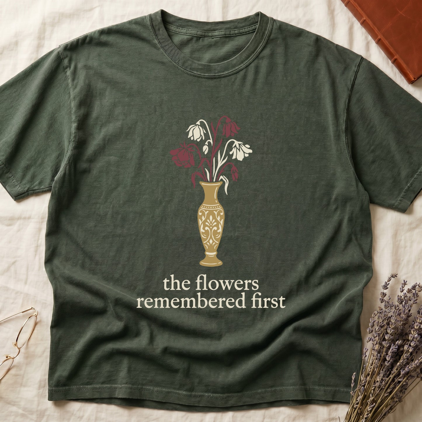 Green tee with gold ornate vase, wilting cream lilies and dark red roses, "the flowers remembered first" in cream serif.