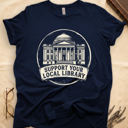 Navy tee with circular cream badge of a classical library building, "SUPPORT YOUR LOCAL LIBRARY" on a banner below.