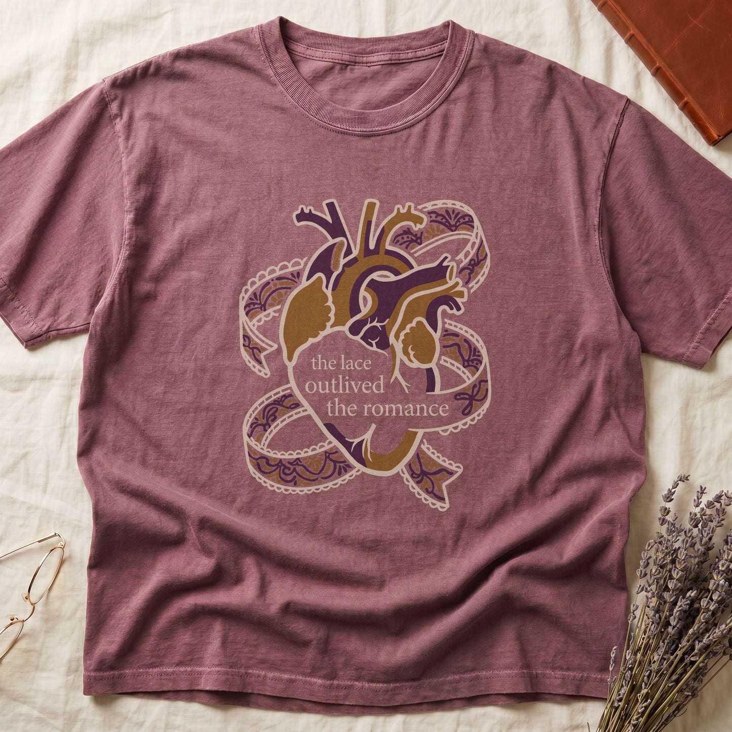 Dark Rose tee with anatomical heart in purple and gold wrapped in lace ribbons, "the lace outlived the romance" in serif.