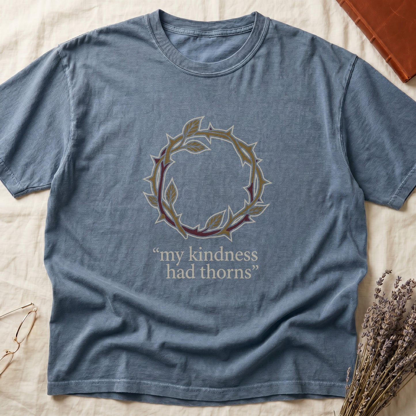 Blue Jean tee with crown of thorns in gold and red with green leaves, "my kindness had thorns" in cream serif.