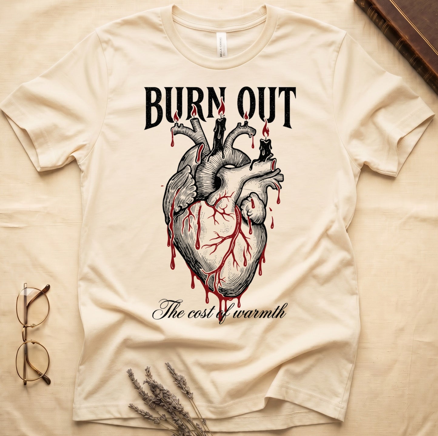 Natural tee with anatomical heart and melted candles dripping red wax, "BURN OUT" top, "The cost of warmth" cursive below.