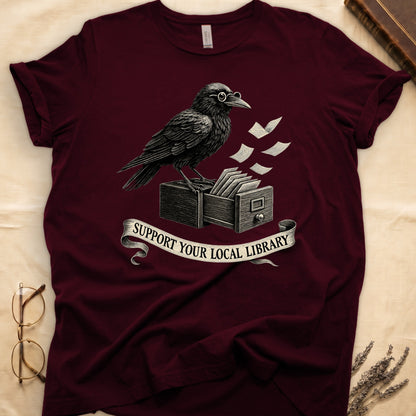 Navy tee with raven writing on "823.4" parchment by candlelight, ink jar beside, "MIDNIGHT CATALOGUER" banner above.