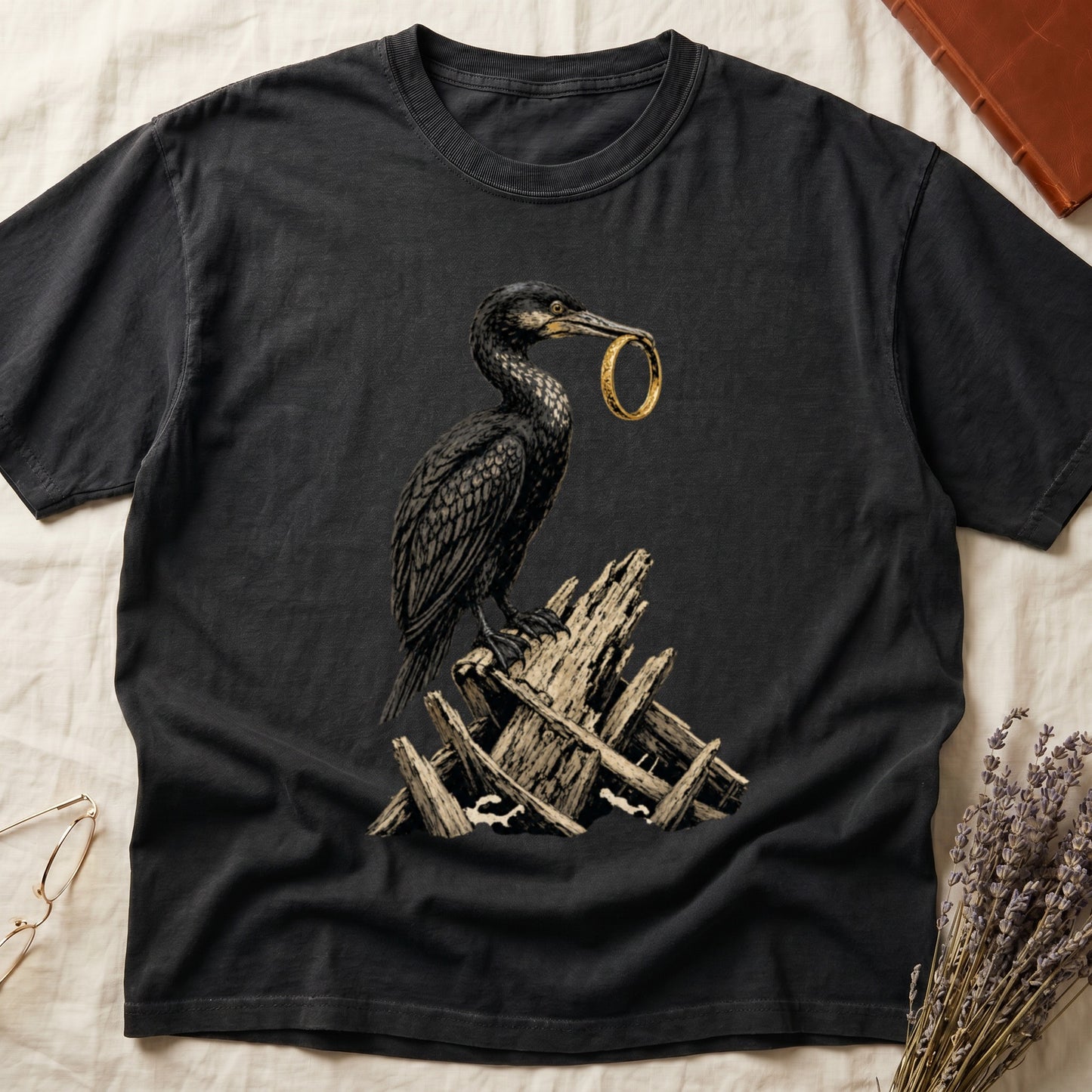 Dark t-shirt featuring a cormorant holding a golden ring, perched on wooden debris.