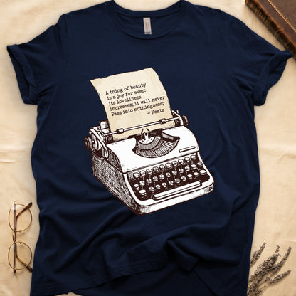 Navy tee with vintage typewriter in cream linework, paper showing "A thing of beauty is a joy for ever" by Keats.
