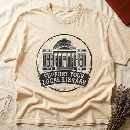 Ivory tee with circular cream badge of a classical library building, "SUPPORT YOUR LOCAL LIBRARY" on a banner below.