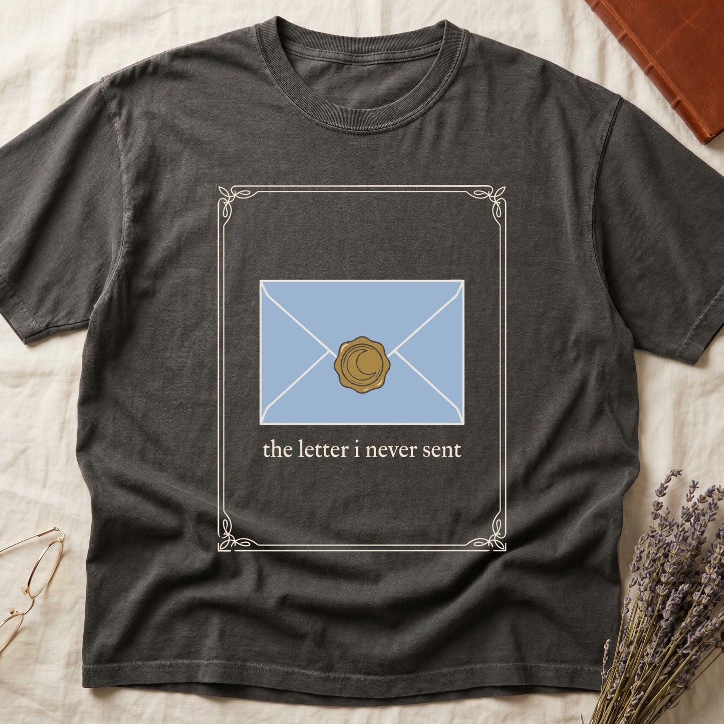 Pepper tee with pale blue envelope sealed with gold crescent moon wax seal, "the letter i never sent" cream serif below.