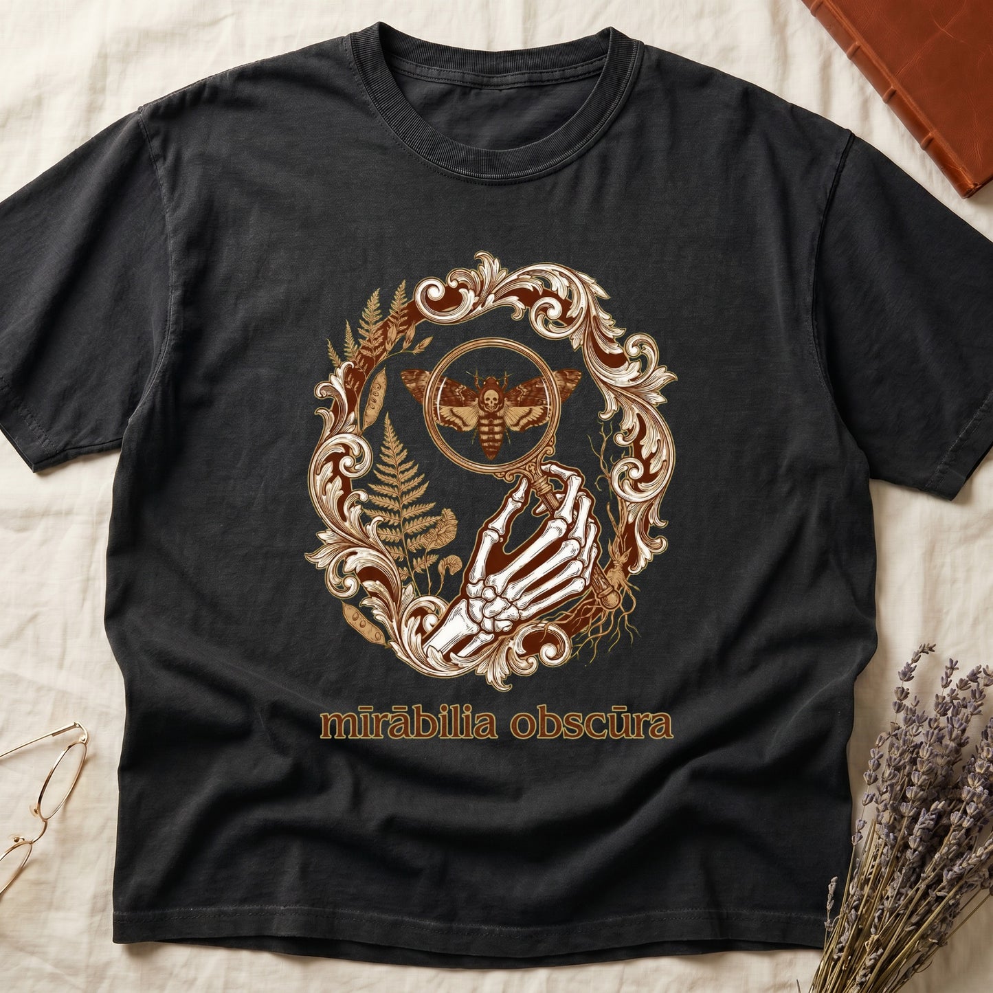 Black tee with skeletal hand, magnifying glass, death's-head moth, ferns on green, "mīrābilia obscūra" in Latin italic.