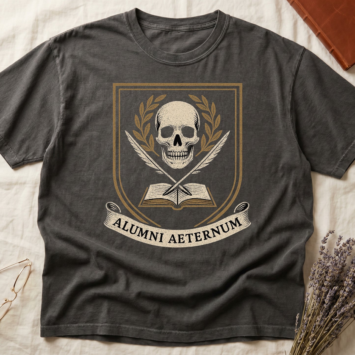 Pepper tee with heraldic shield, skull and gold laurels, crossed quills, open book, scroll "ALUMNI AETERNUM" below.