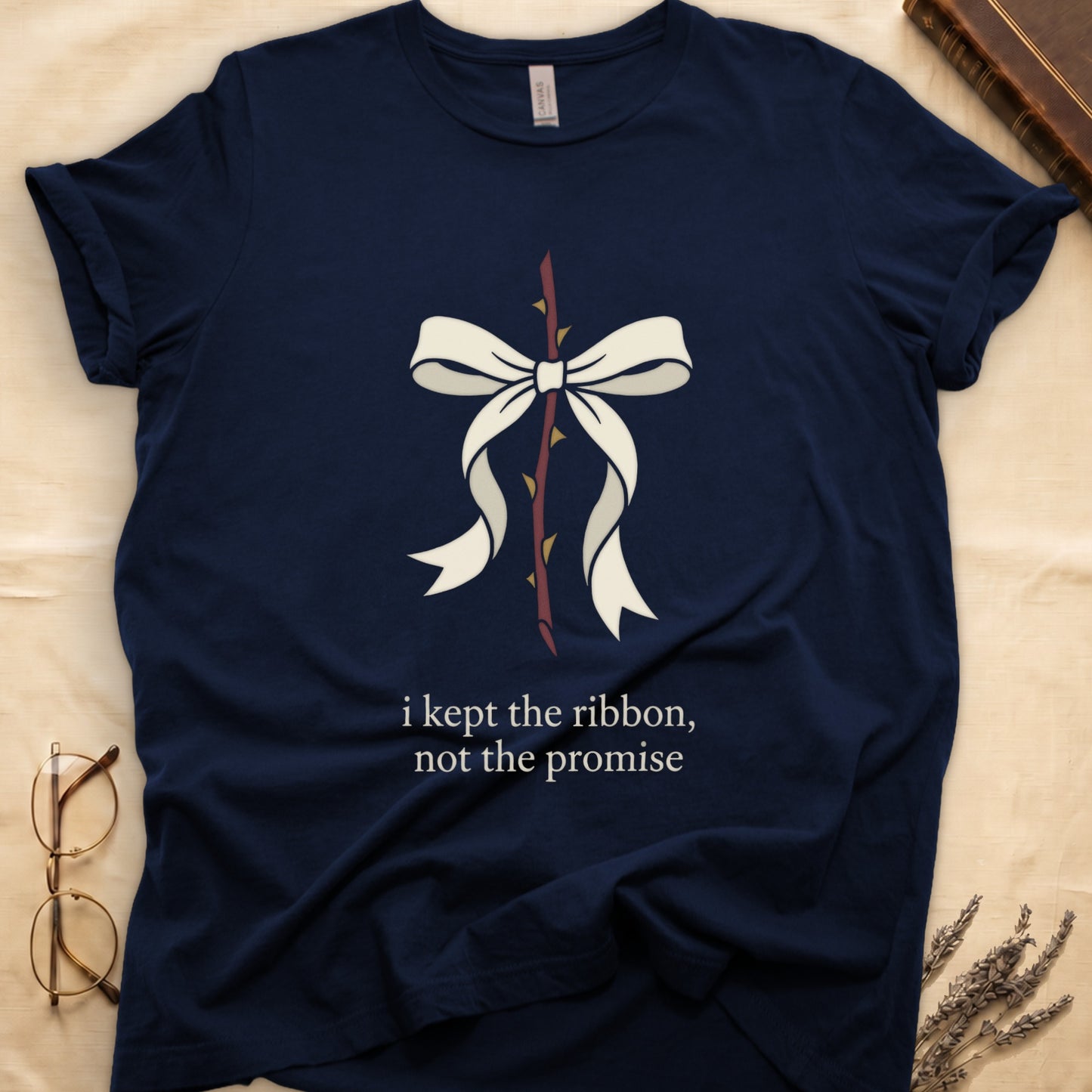 Navy tee with cream bow tied around thorny rose stem, "i kept the ribbon, not the promise" in cream serif below.