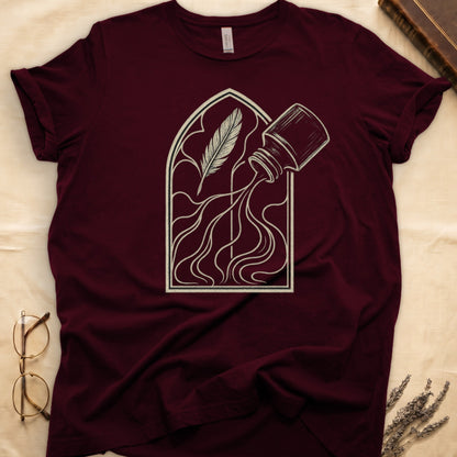 Maroon tee with sepia gothic arch, feather quill on left and tipped ink bottle on right spilling ink in curling tendrils.