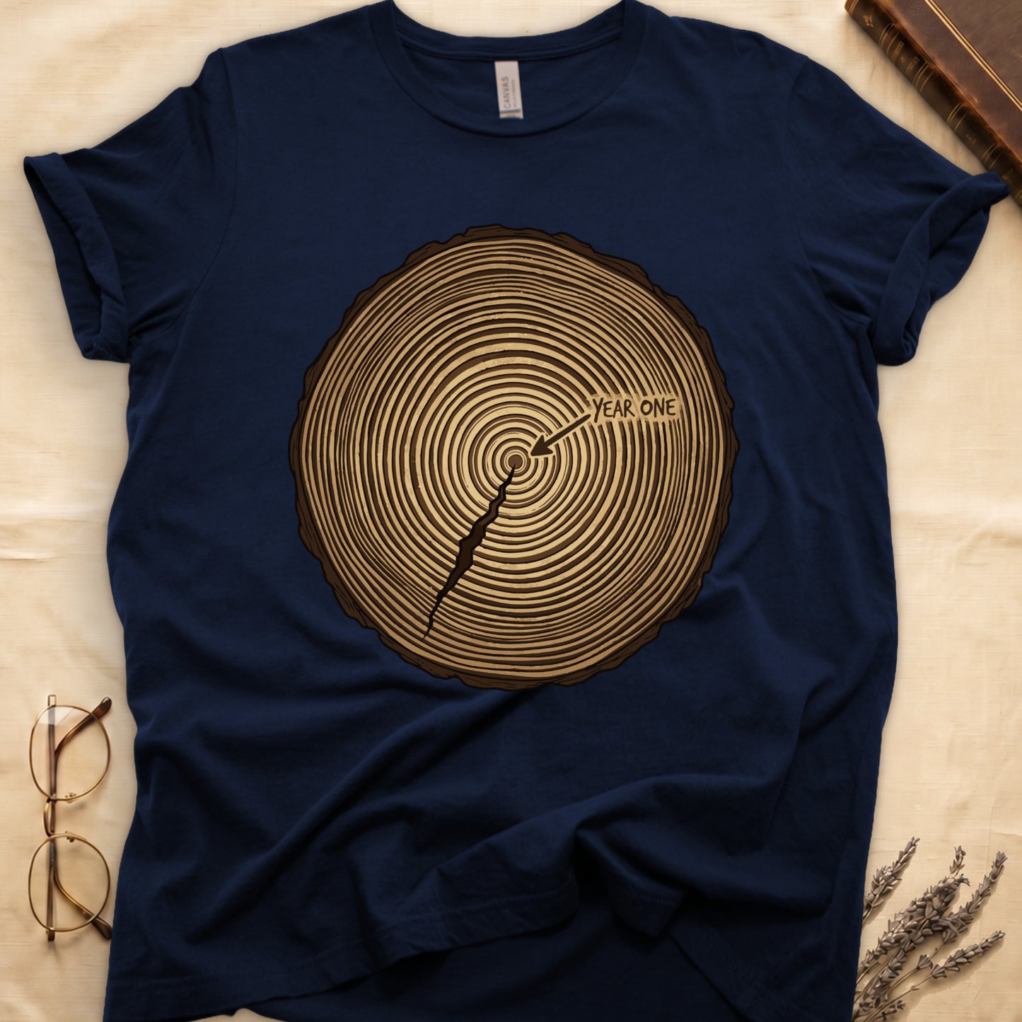 Navy tee with cross-section of tree rings in warm brown, arrow pointing to center labeled "YEAR ONE" in serif type.