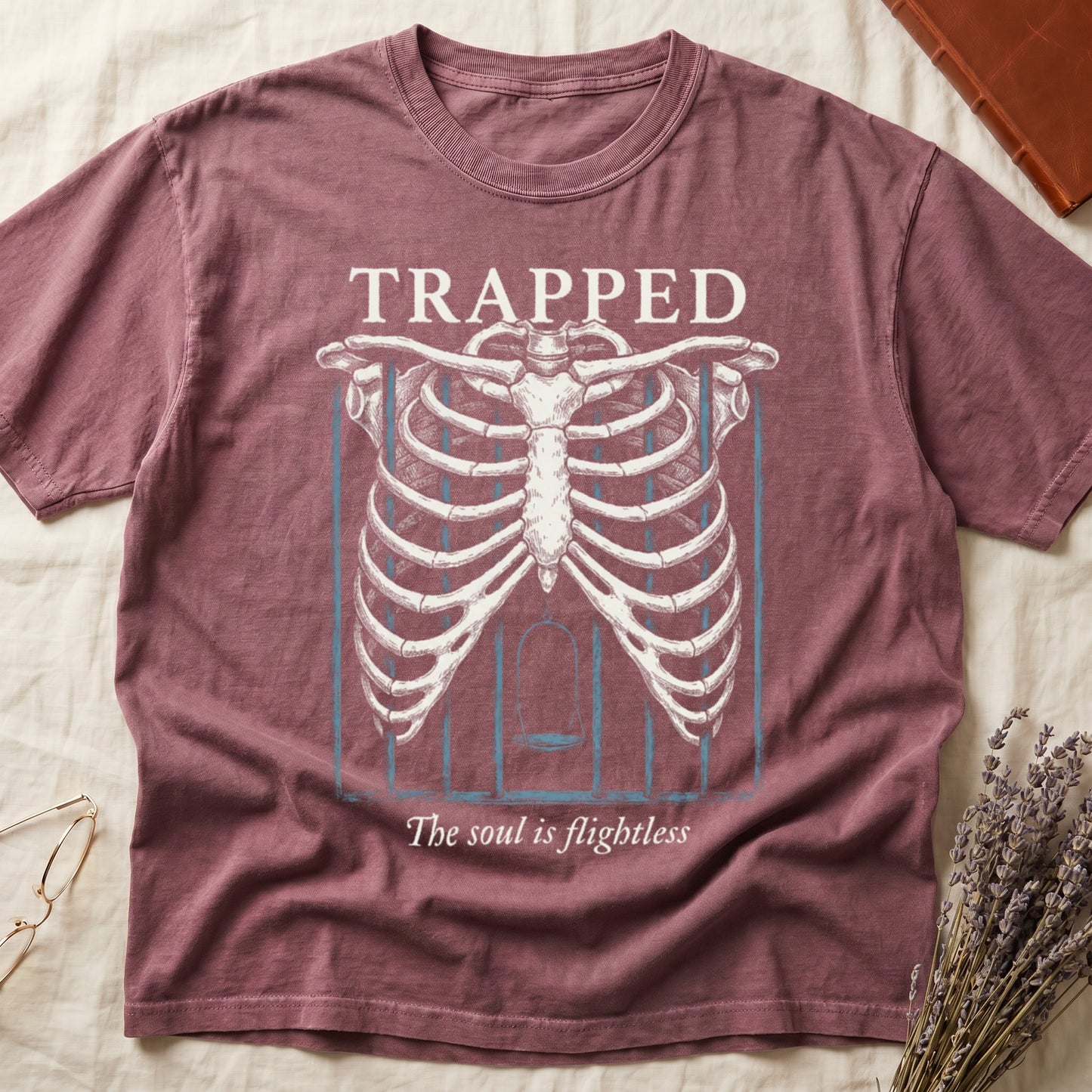 Dark Rose tee with anatomical ribcage on prison bars, bird swing inside, "TRAPPED" top, "The soul is flightless" italic below.
