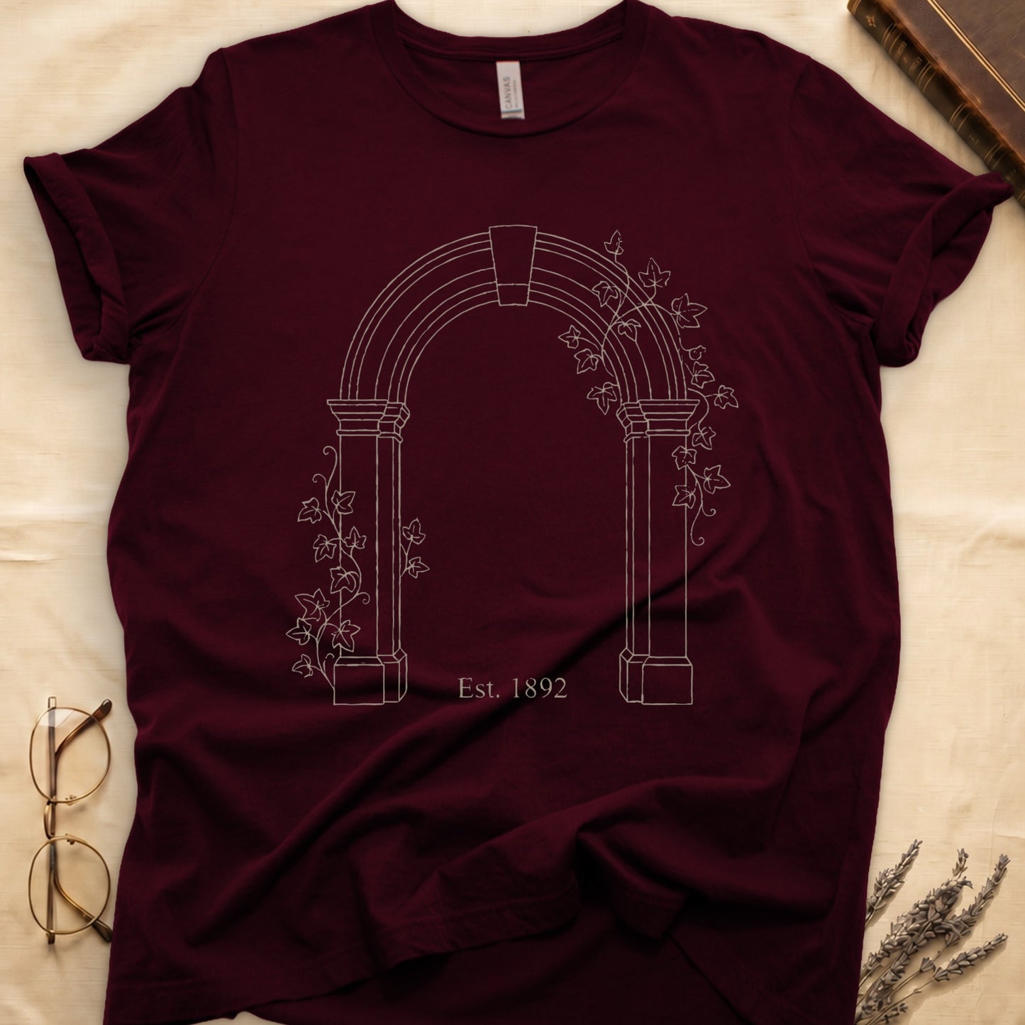 Maroon tee with Gothic stone archway in cream linework, ivy climbing the columns, "Est. 1892" inscribed at the base.