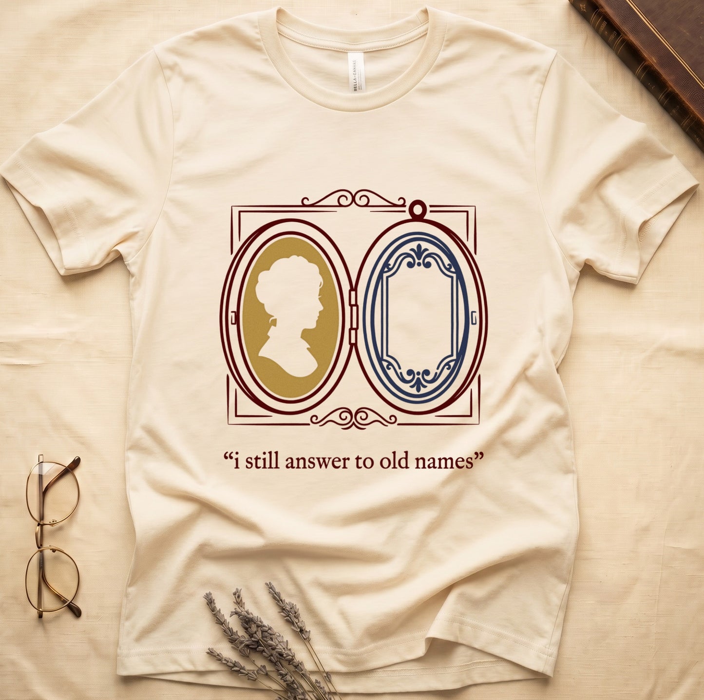 Natural tee with Victorian double-locket, silhouette portrait in gold frame, "i still answer to old names" cream serif below.