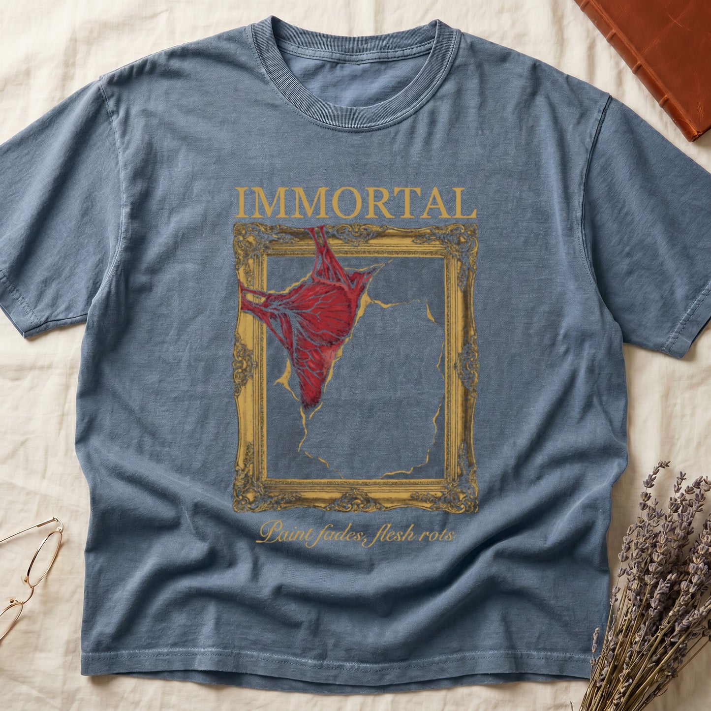 Blue Jean tee with gold frame and exposed muscle tearing canvas, "IMMORTAL" top, "Paint fades, flesh rots" italic below.