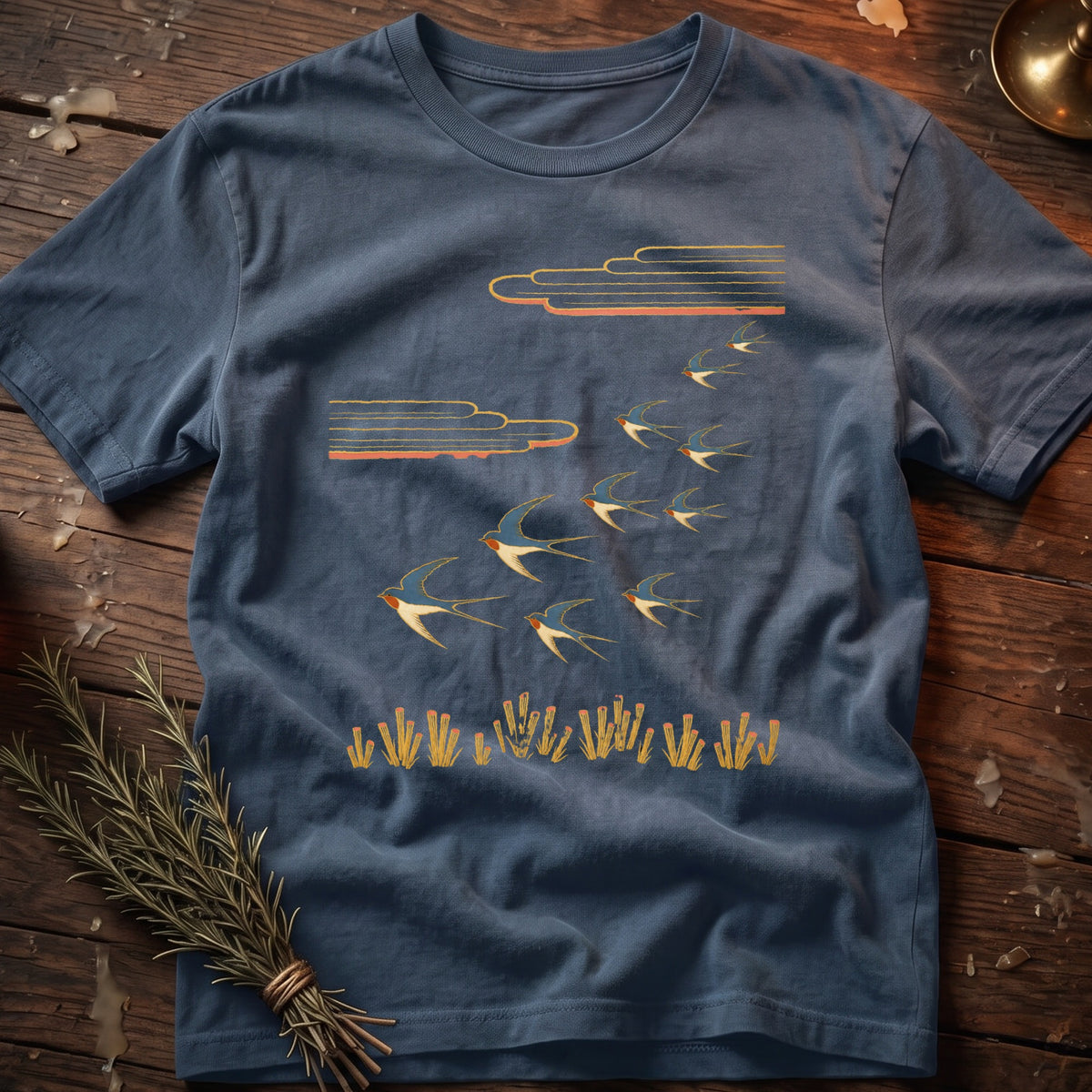Blue t-shirt with swallows flying near clouds and stalks of grass.