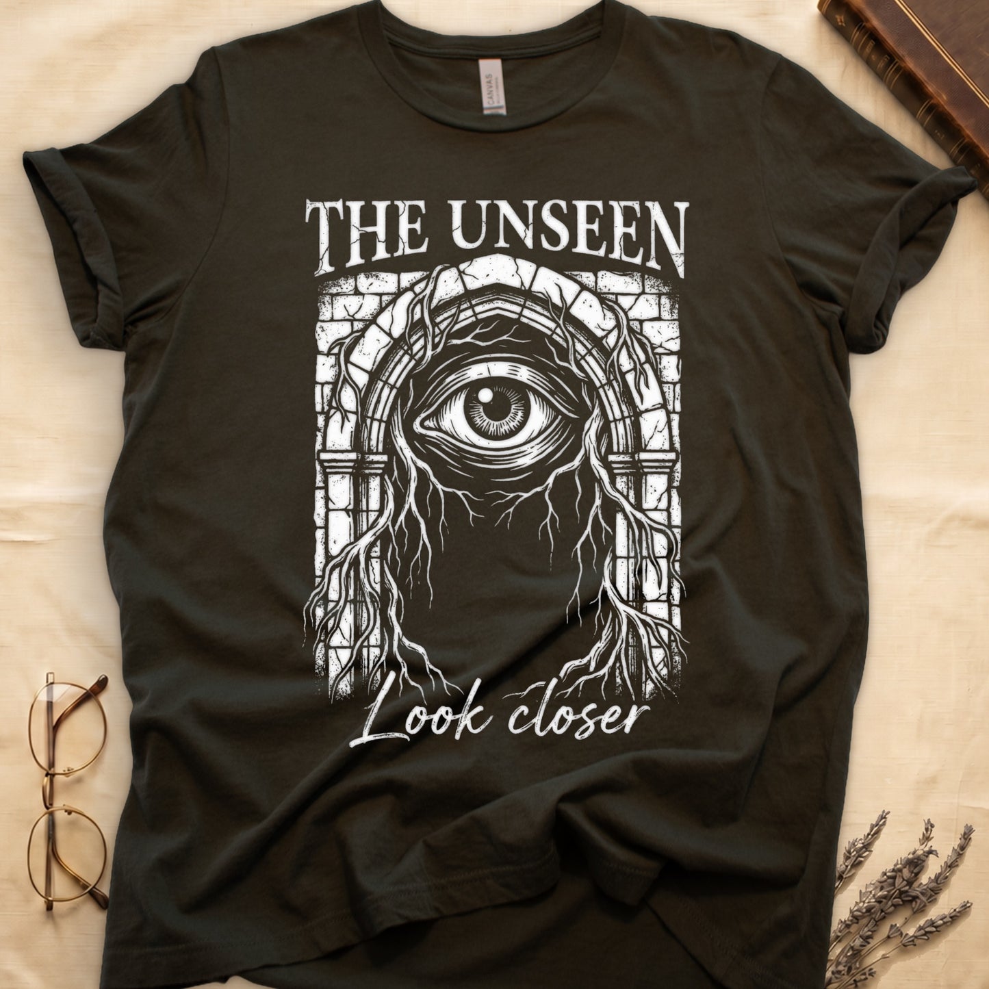 Military Green tee with Gothic stone arch, open eye, roots trailing, "THE UNSEEN" top, "Look closer" cursive below.