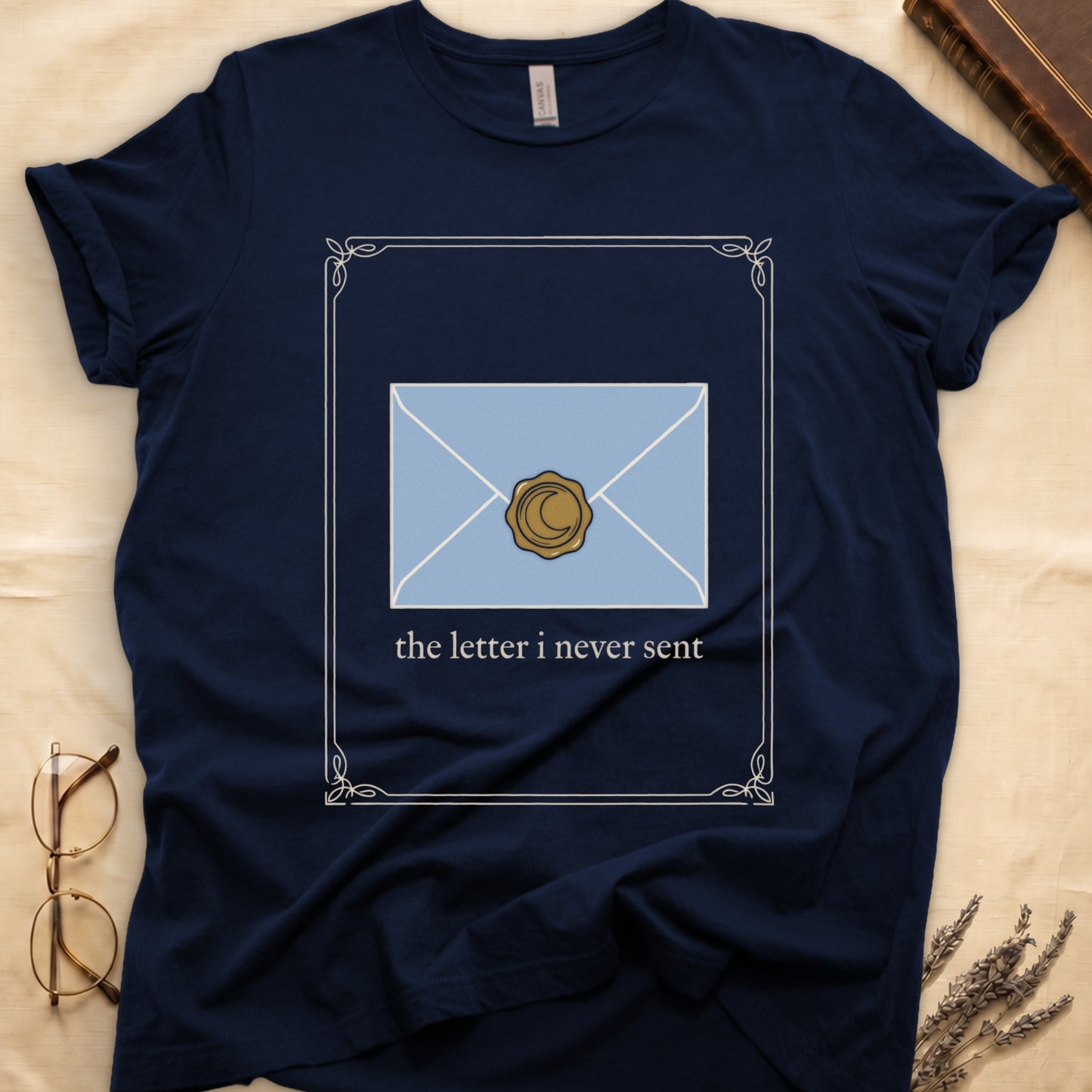 Navy tee with pale blue envelope sealed with gold crescent moon wax seal, "the letter i never sent" cream serif below.