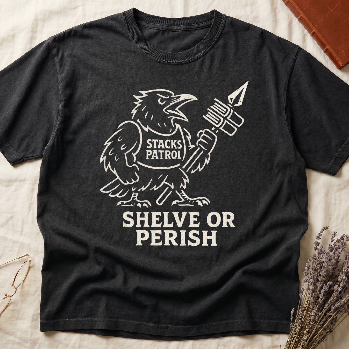 Black tee with vintage raven mascot, "STACKS PATROL" sash, feather pen aloft, "SHELVE OR PERISH" bold serif below.