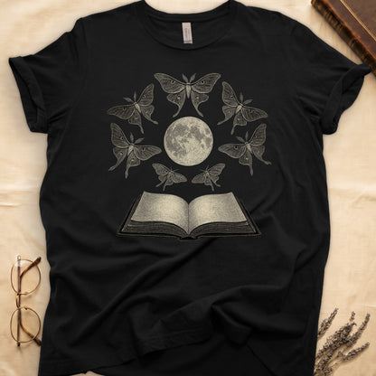 Black tee with full moon center, seven luna moths in halo around, open book below, cream-on-black engraving.