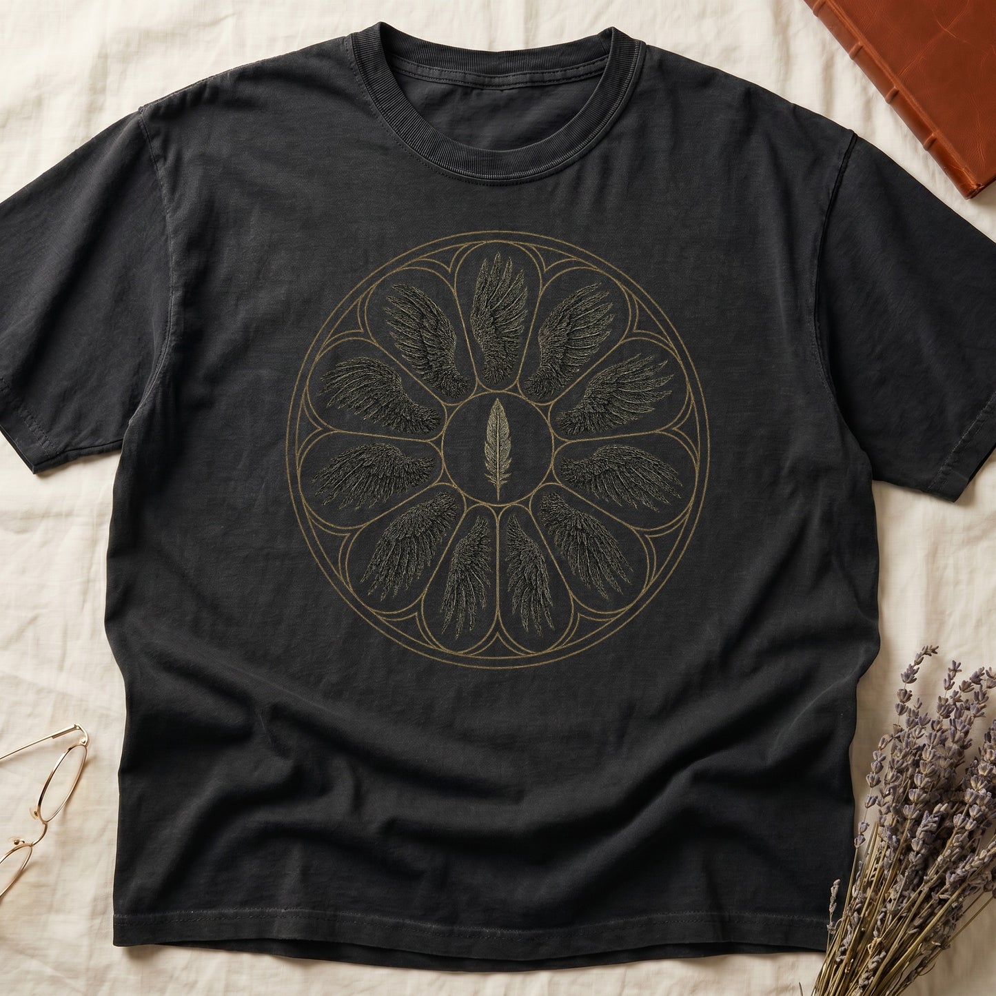 Black tee with sepia rose-window of eight feathered wings around central feather, engraved linework on parchment ground.
