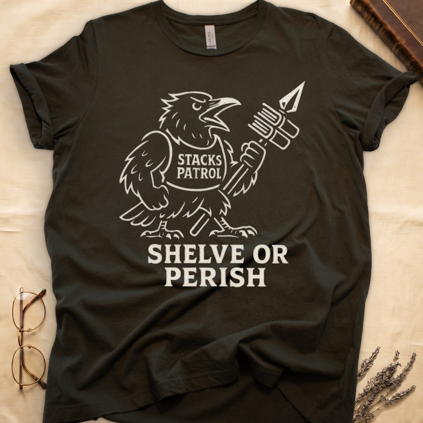 Military Green tee with vintage raven mascot, "STACKS PATROL" sash, feather pen aloft, "SHELVE OR PERISH" bold serif below.